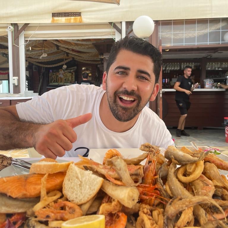 Ali steekt zijn duim op bij een schaal zeevruchten op een terras