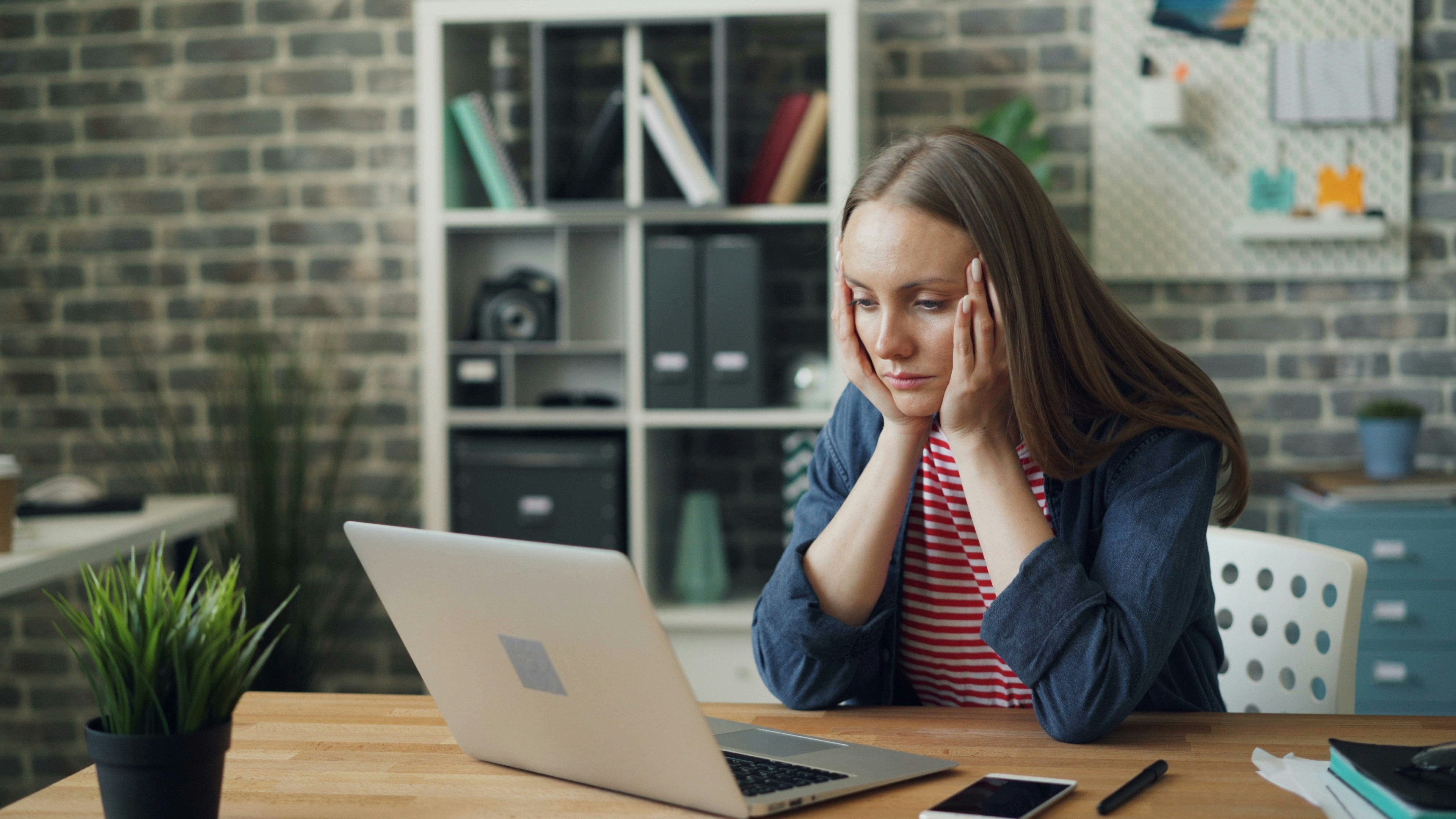 Tired young woman using laptop in office touching head feeling headache