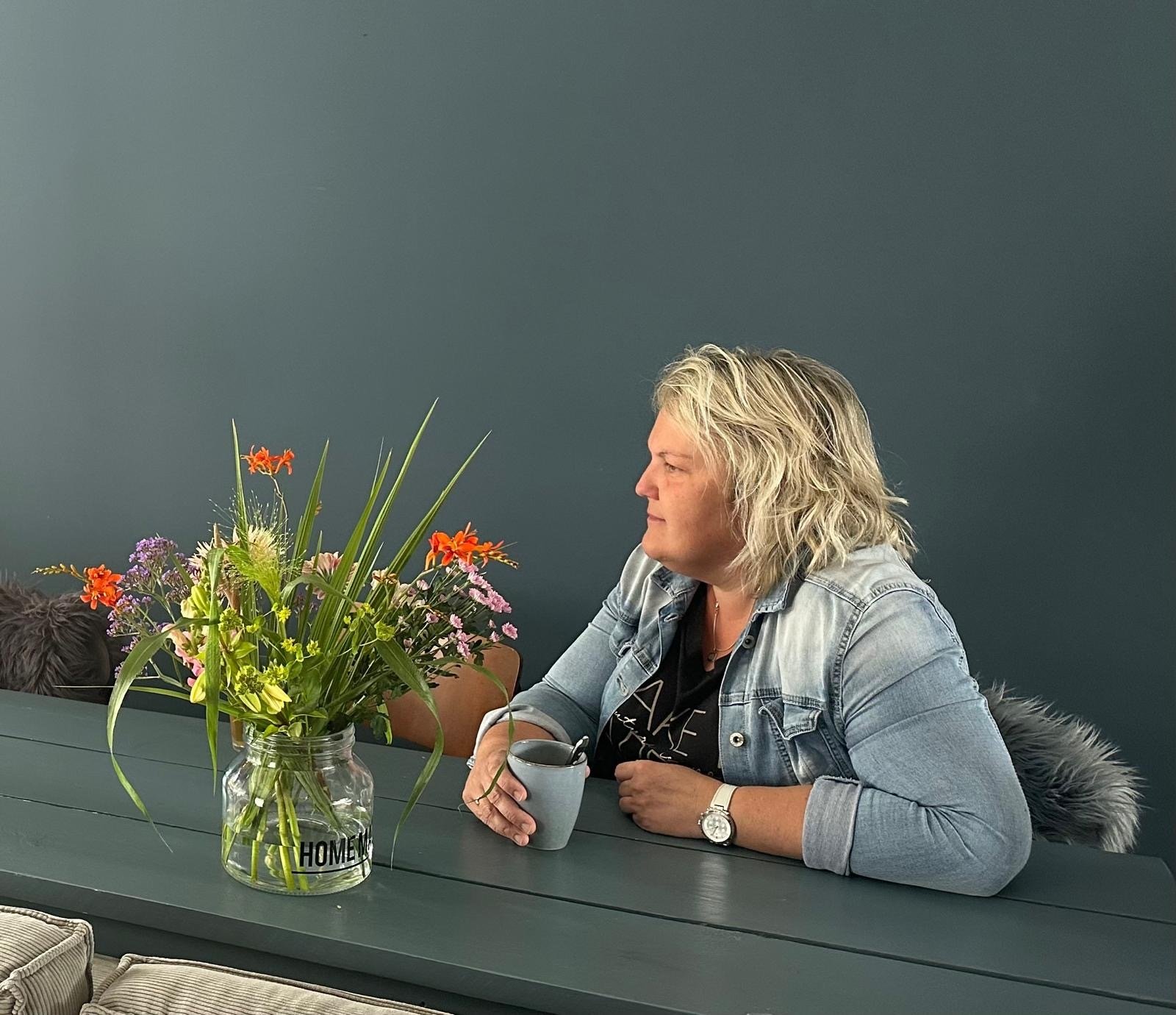 Portret van Petra Komdeur, spreker over afscheid en informele uitvaartzorg, aan tafel met bloemen