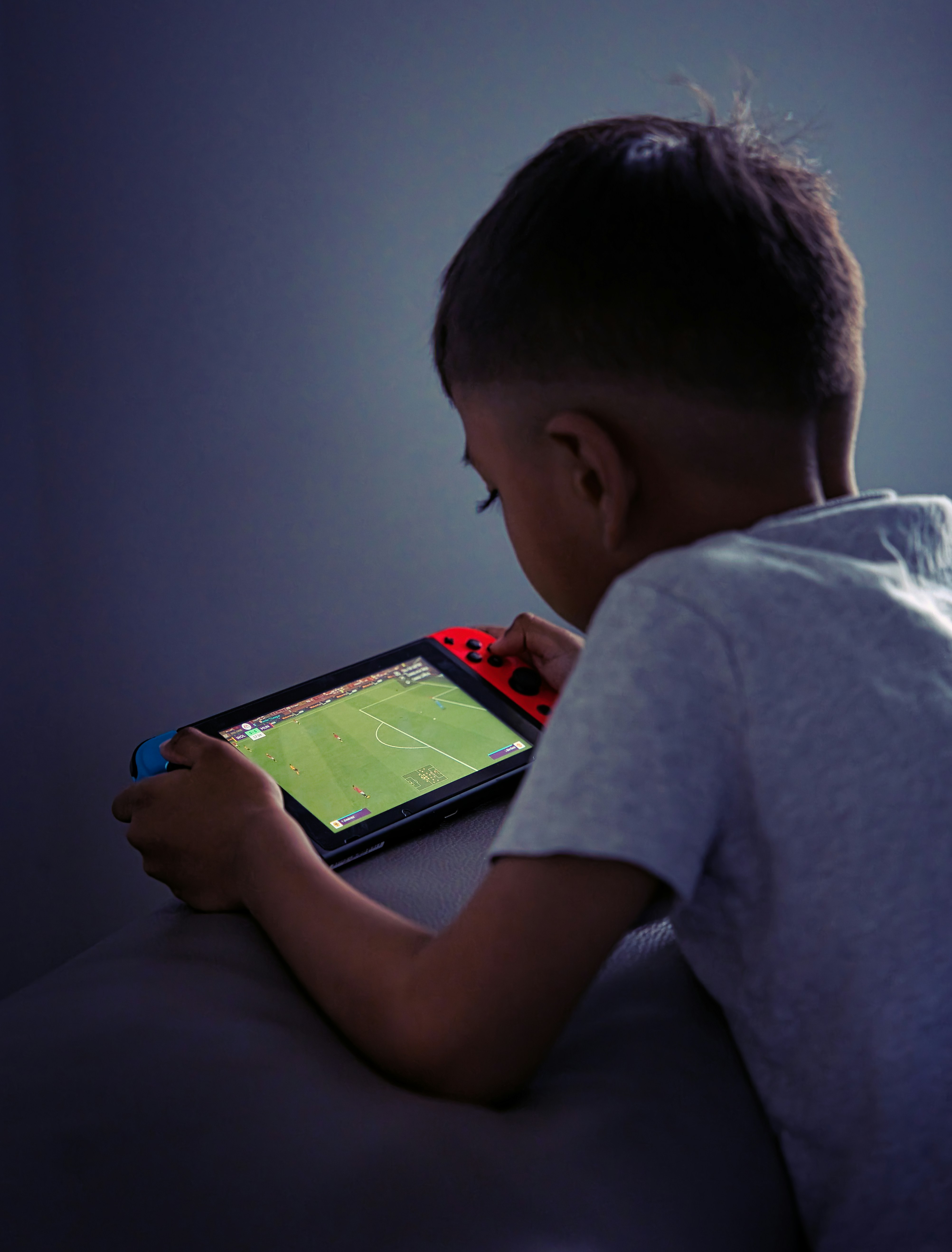 Young boy playing on a Nintendo Switch with a soccer field on the screen - FIFA Football