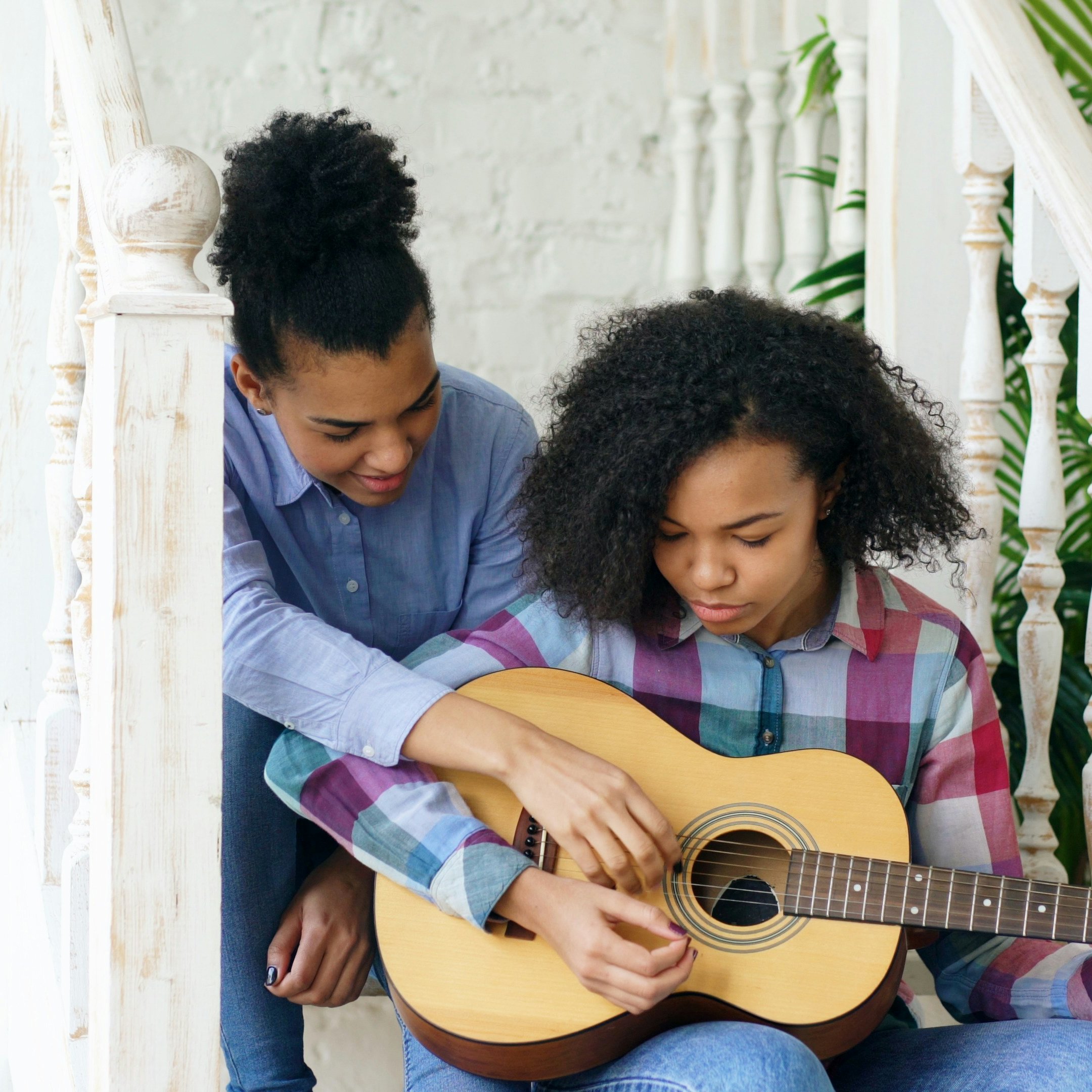 Mixed race young woman sitting on stairs teaching her teenage sister to play acoustic guitar