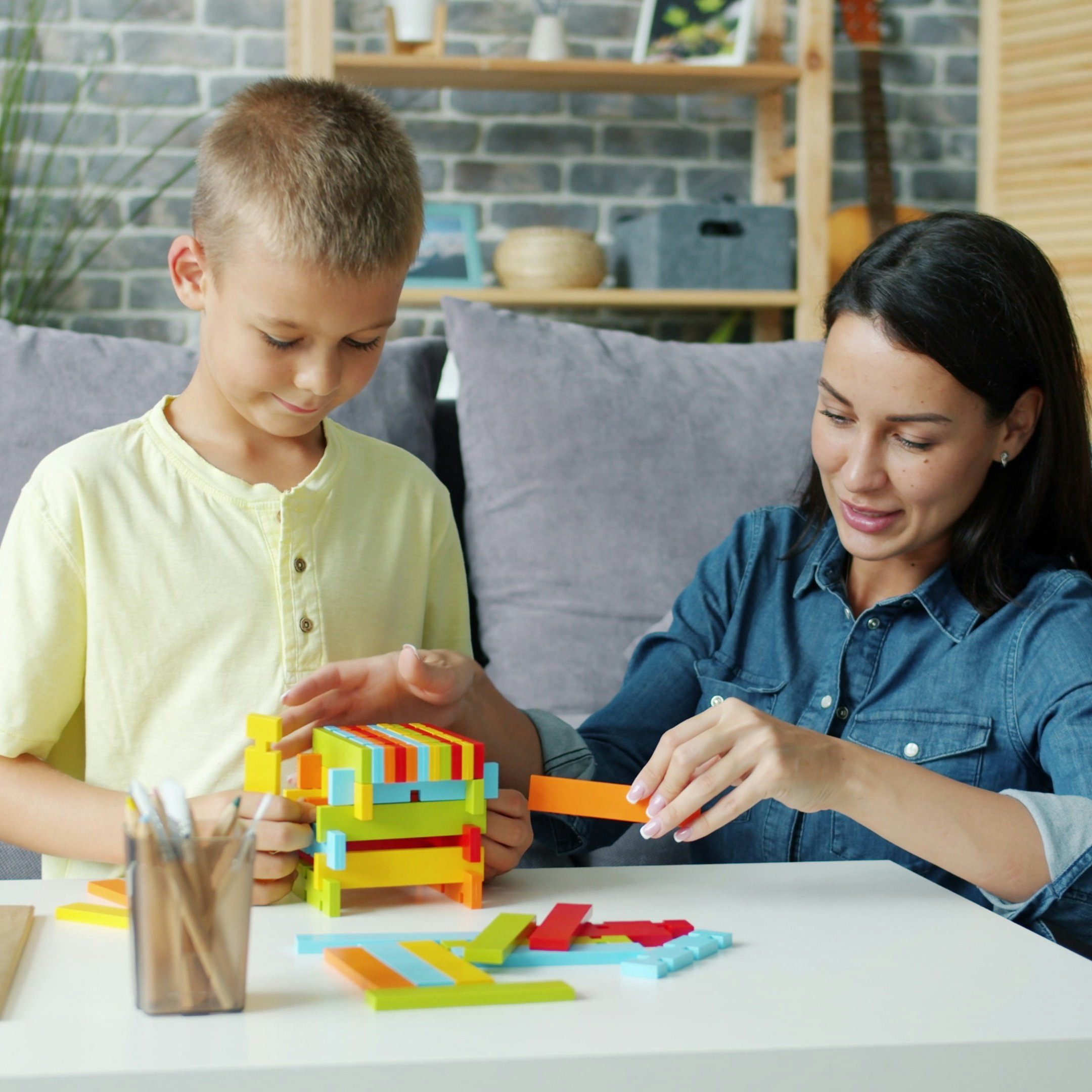 Cheerful girl mother is playing with little son with wooden blocks and laughing enjoying educational activity. Happy family, people and interesting toys concept.