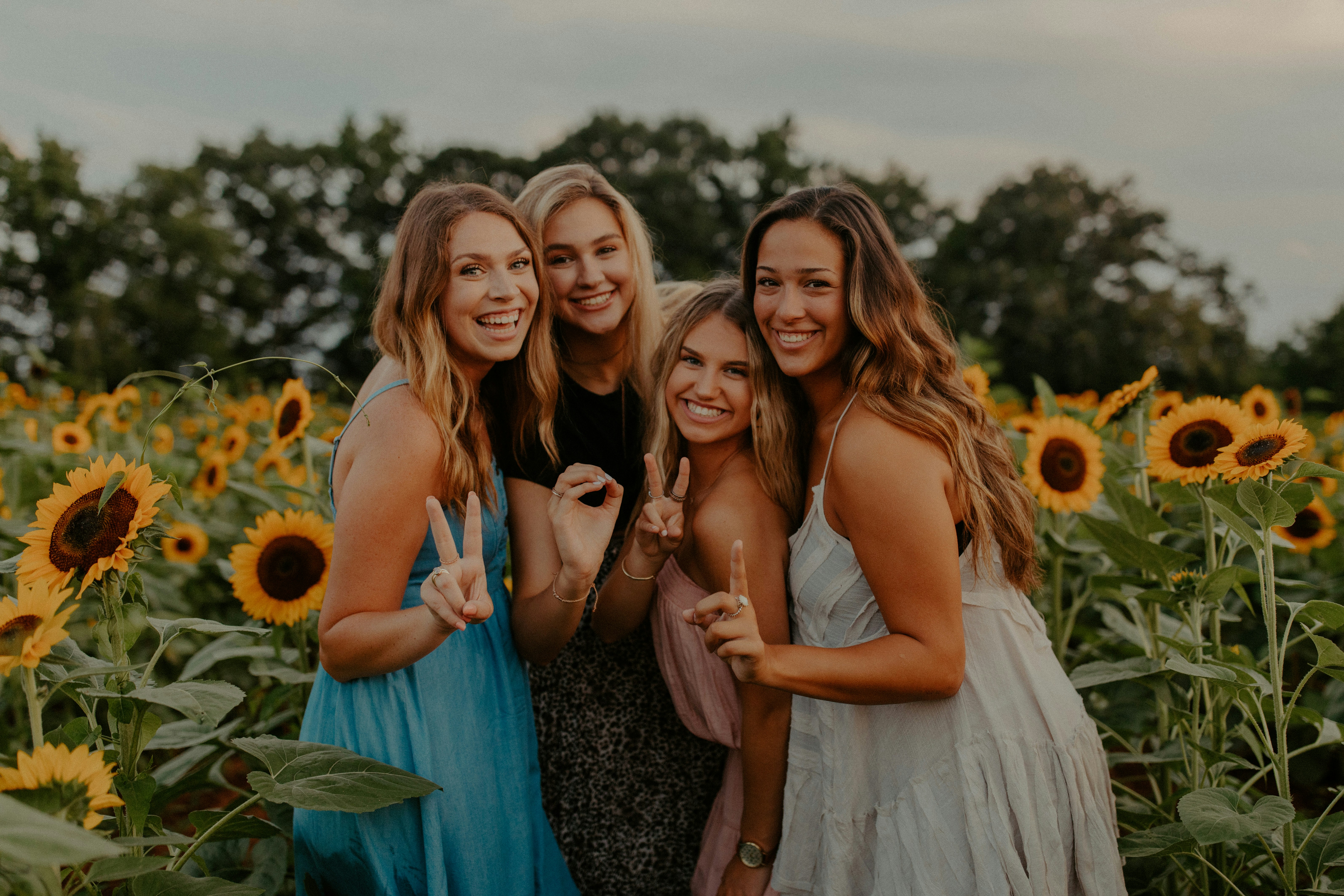 christian girls laughing together holding hands in the air in a sunflower field spelling out 2021