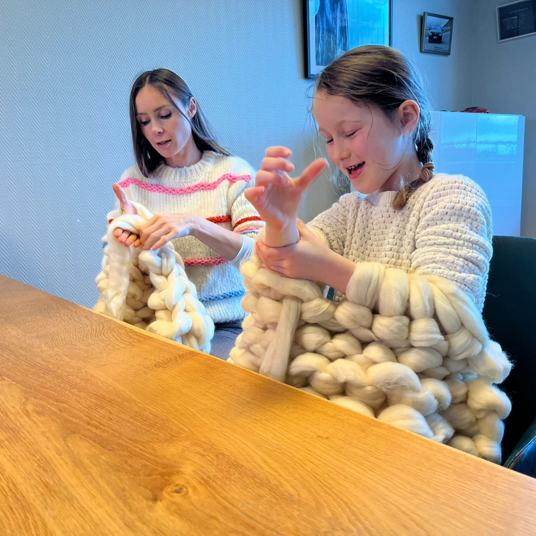 Moeder en dochter breien samen een deken met lontwol.