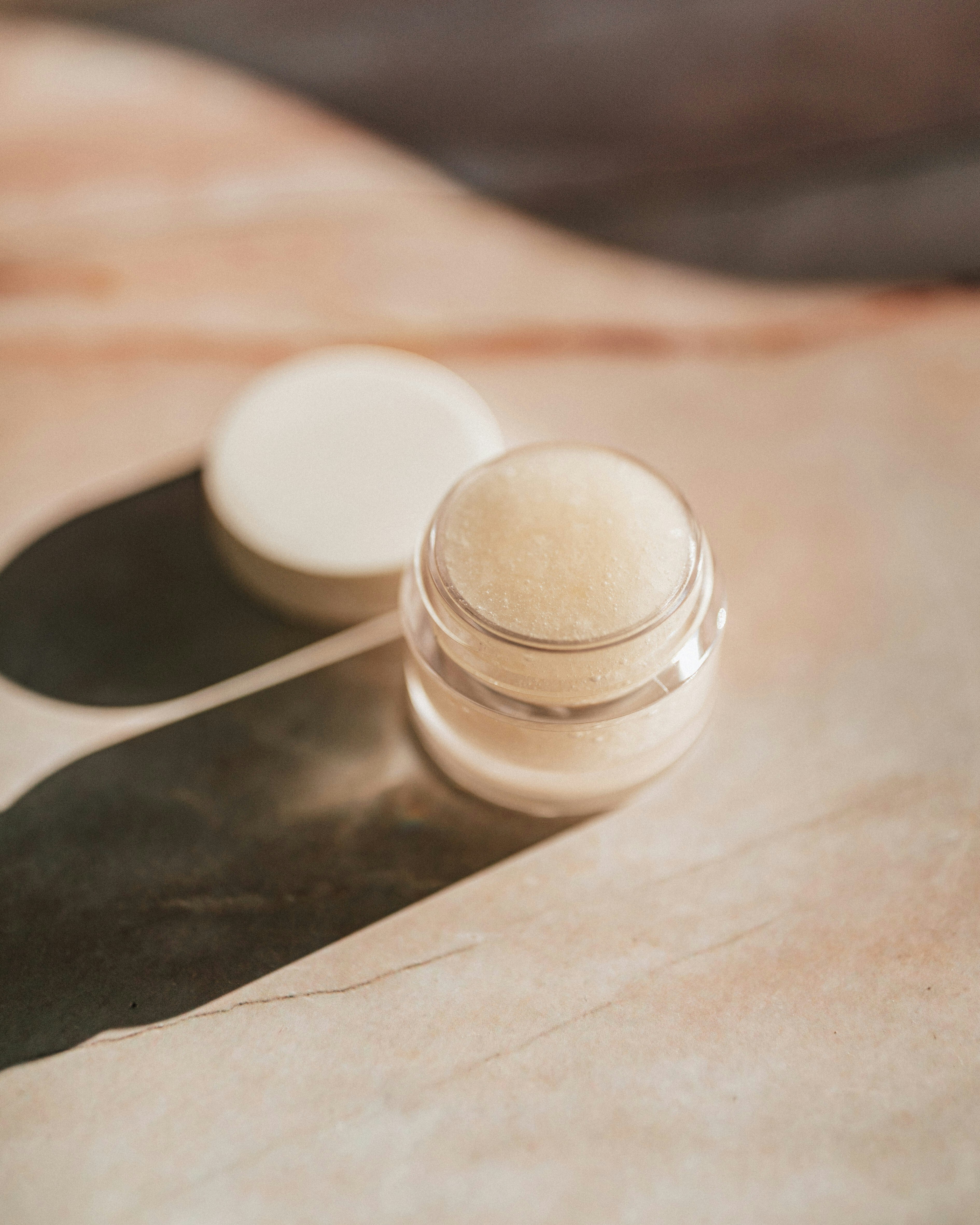 Doorzichtig sample potje met een korrelachtige beige inhoud. De witte deksel ligt naast de sample pot op een houten ondergrond. Korean skincare | Een aanvulling voor de bruine huid?