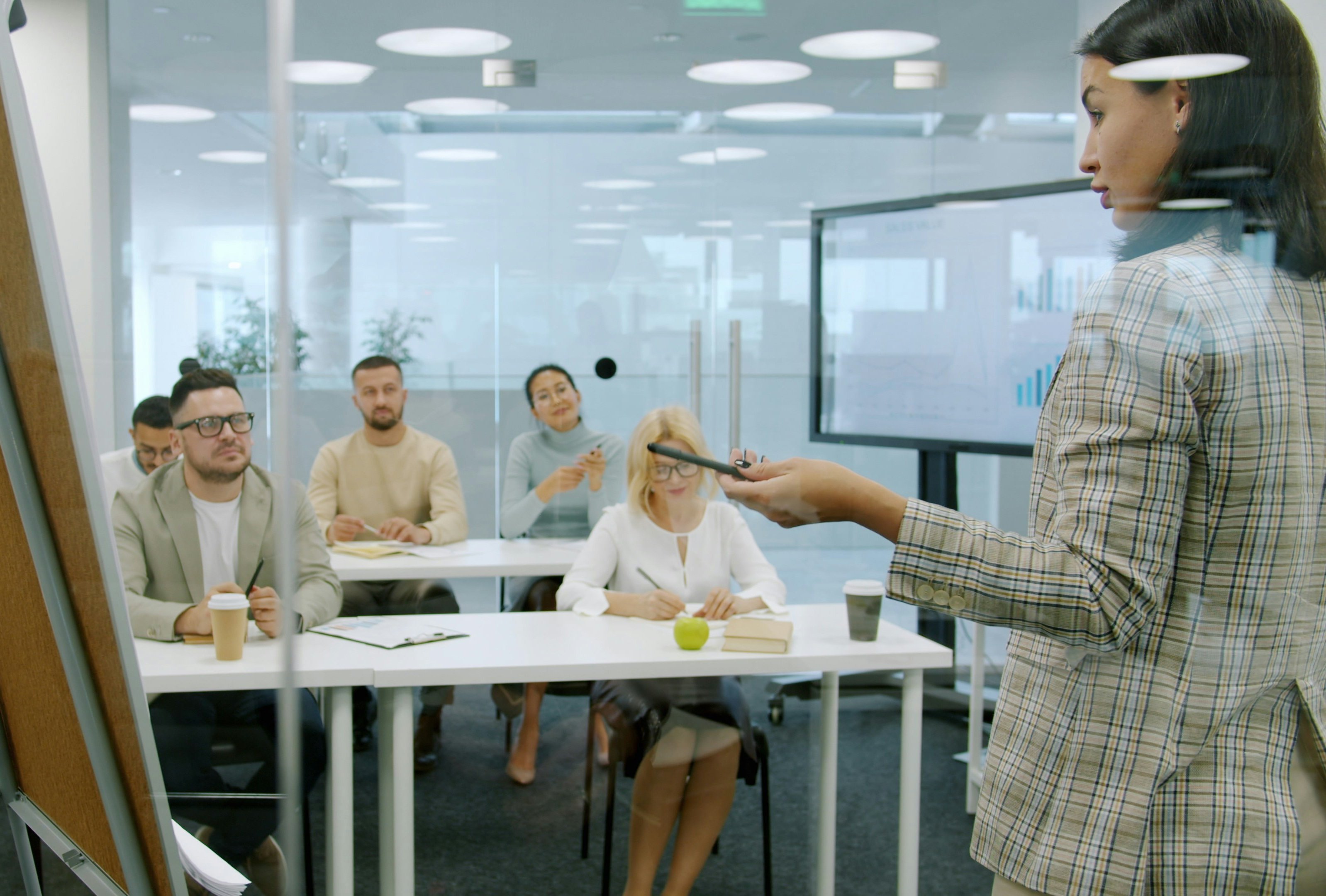 Managers men and women are listening to employee young lady making report in conference room talking and gesturing using flipchart whiteboard.