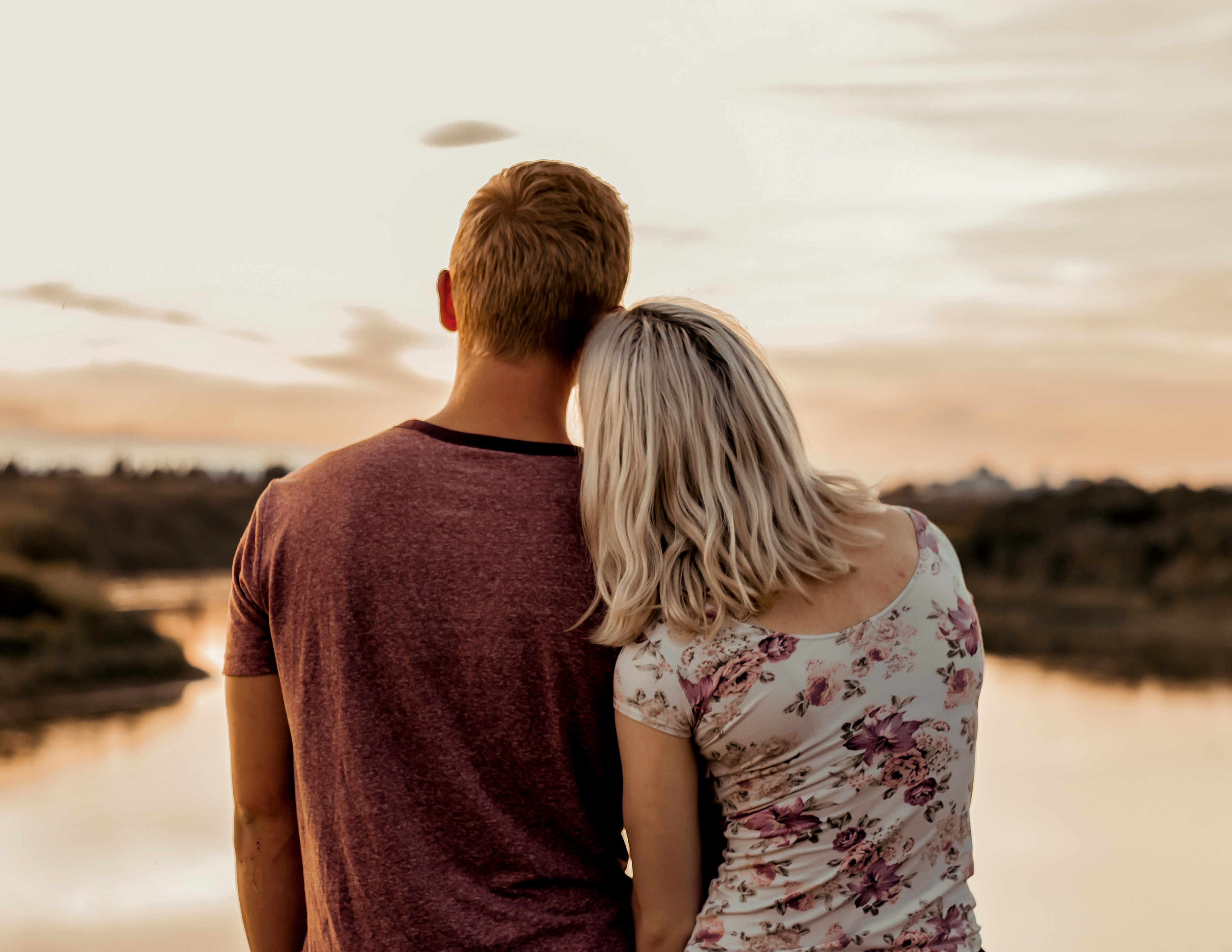Couple holding hands during sunset on a beach looking off toward the water.