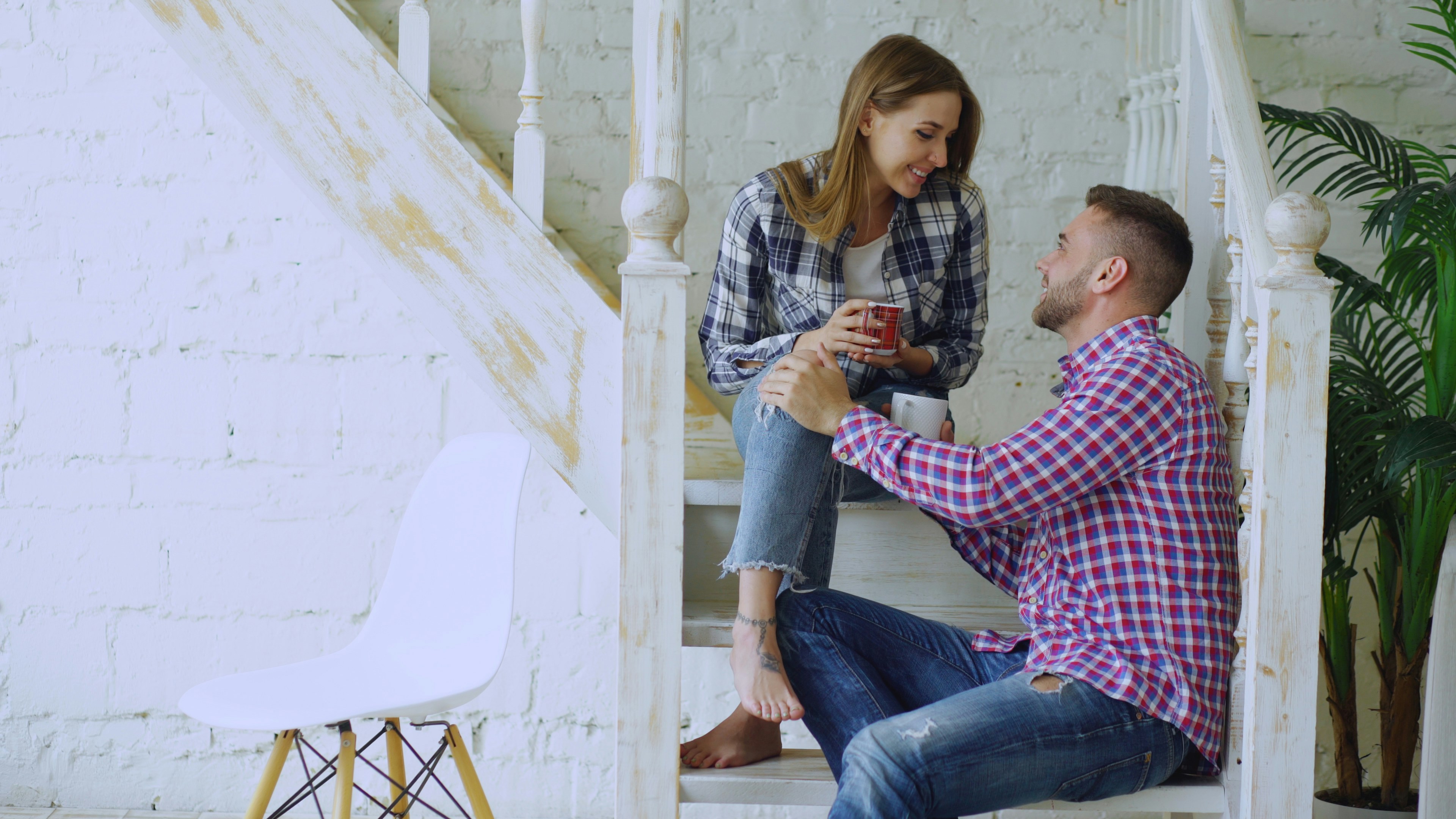 Young happy and loving couple drink tea and talking while sitting on stairs in bedroom at home
