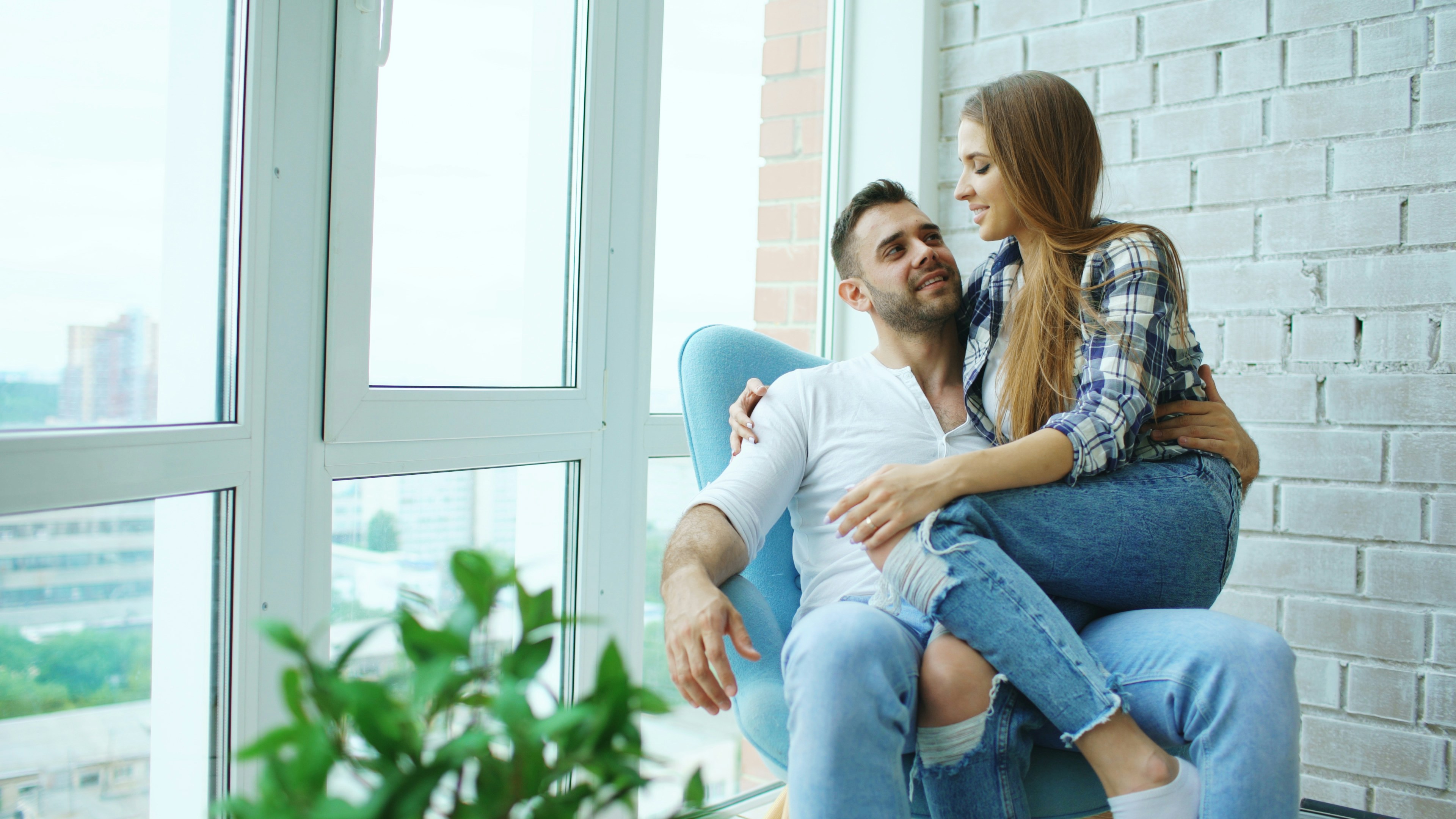 Beautiful young couple relax after relocation sitting on chair and enjoying view from balcony of new loft apartment
