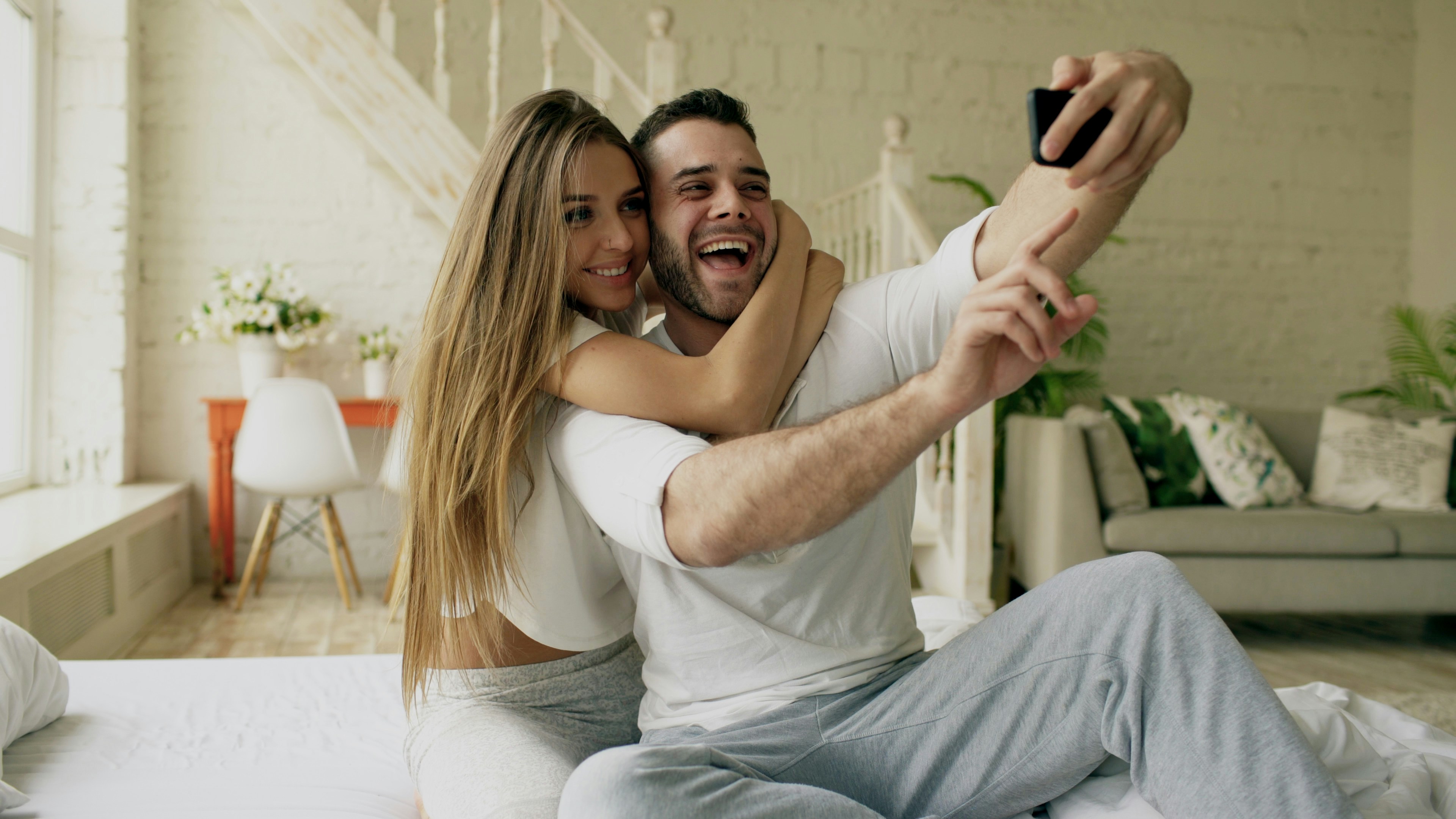 Young beautiful and loving couple take selfie picture on smartphone camera while lying in bed at morning