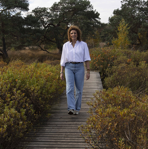 Nicole van Wieringen loopt rustig over een houten brug in het bos, symbool voor stappen zetten naar rust, balans en herstel.
