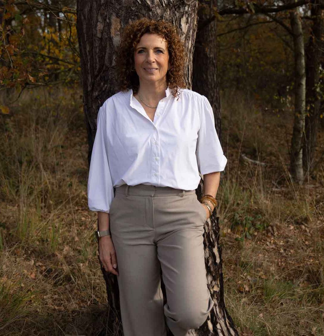 Nicole die ontspannen tegen een boom leunt in de natuur, als symbool voor rust, grounding en innerlijke balans.