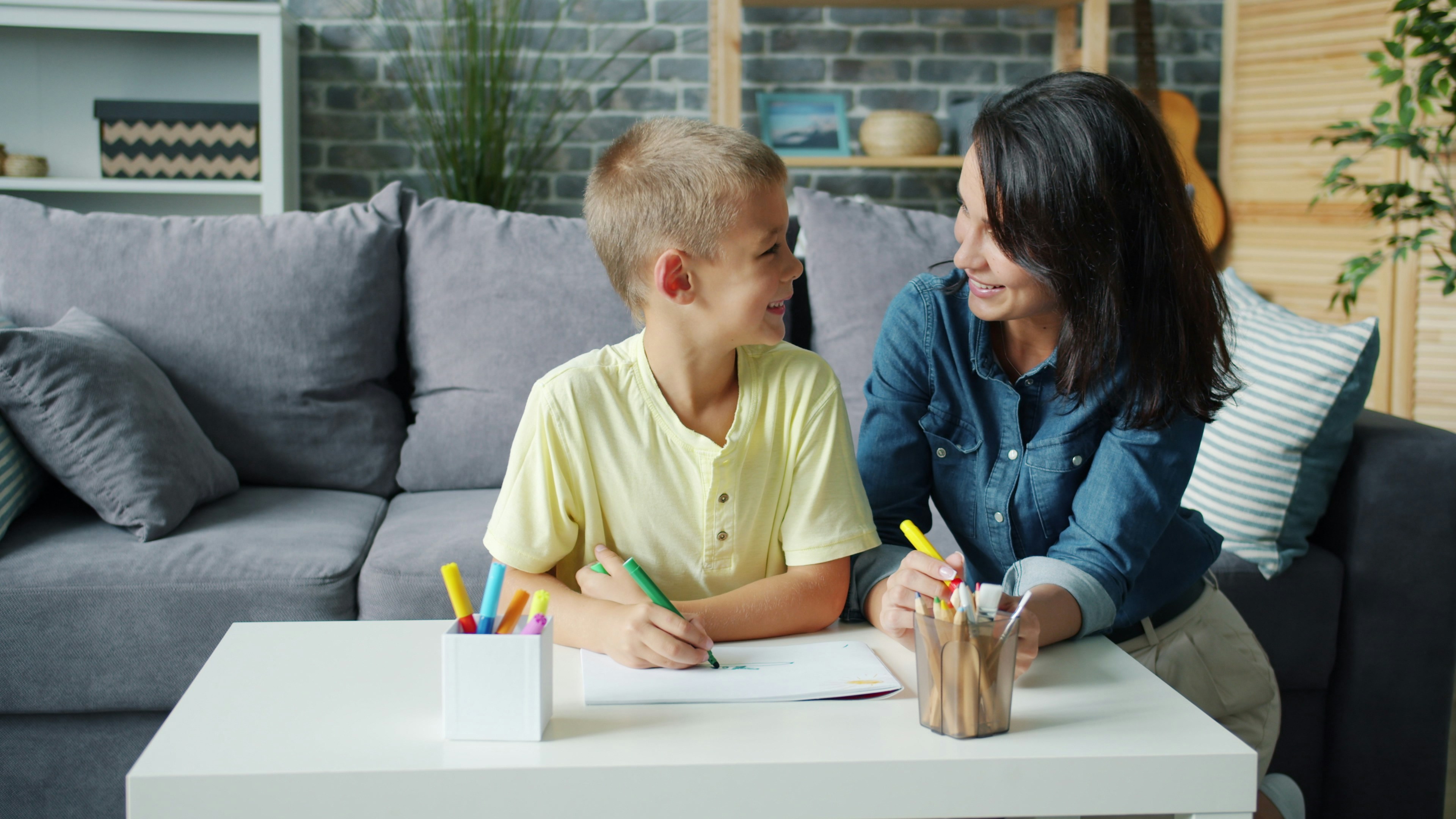 Young woman and happy kid adorable boy are drawing picture at home bonding enjoying hobby in modern cozy apartment. People, family and motherhood concept.