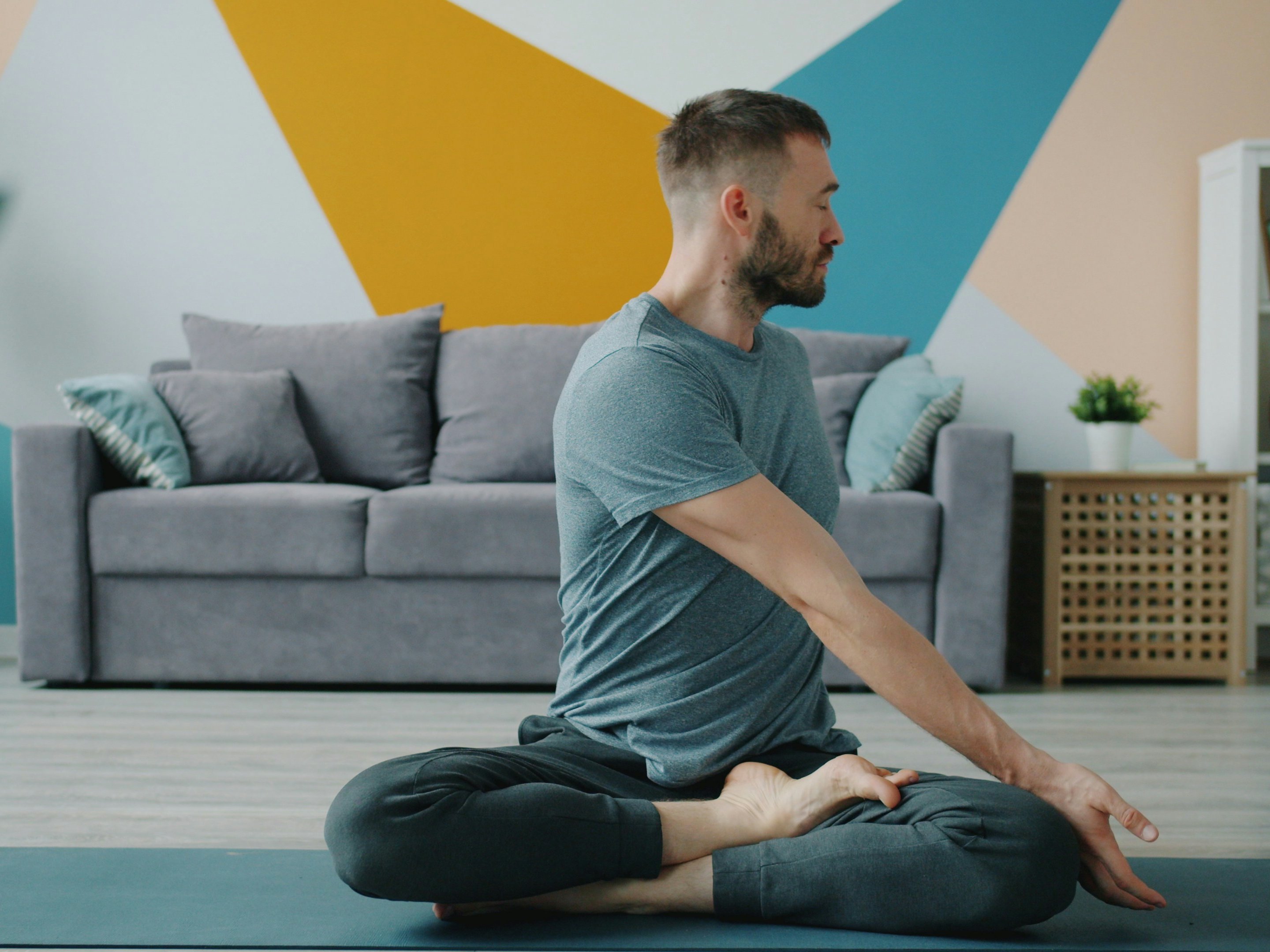 Carefree person good-looking bearded man is doing yoga at home warming-up body sitting in lotus position twisting spine. People and healthcare concept.