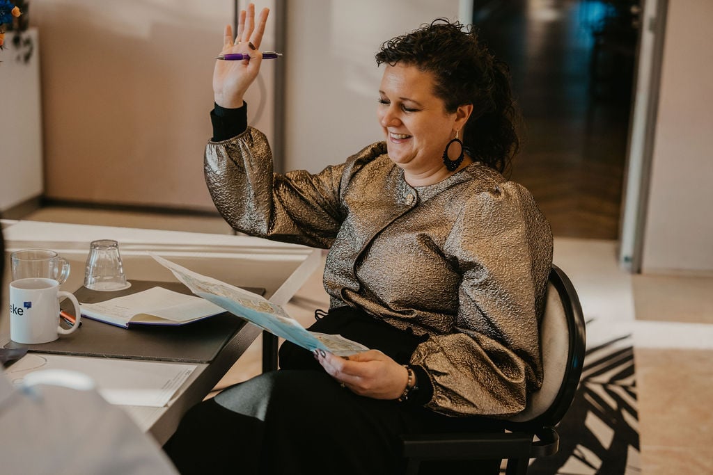 Vrouw met opgeheven hand tijdens training, glimlachend met een planning in de hand, symbool voor overzicht, zelfvertrouwen en eigenaarschap over je tijd