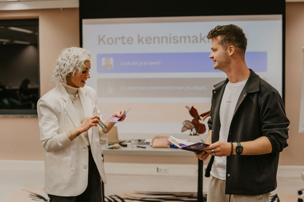 Twee deelnemers in gesprek tijdens een presentatieoefening, met kaarten in de hand en een glimlach, symbool voor zelfverzekerd spreken en verbinding met je publiek