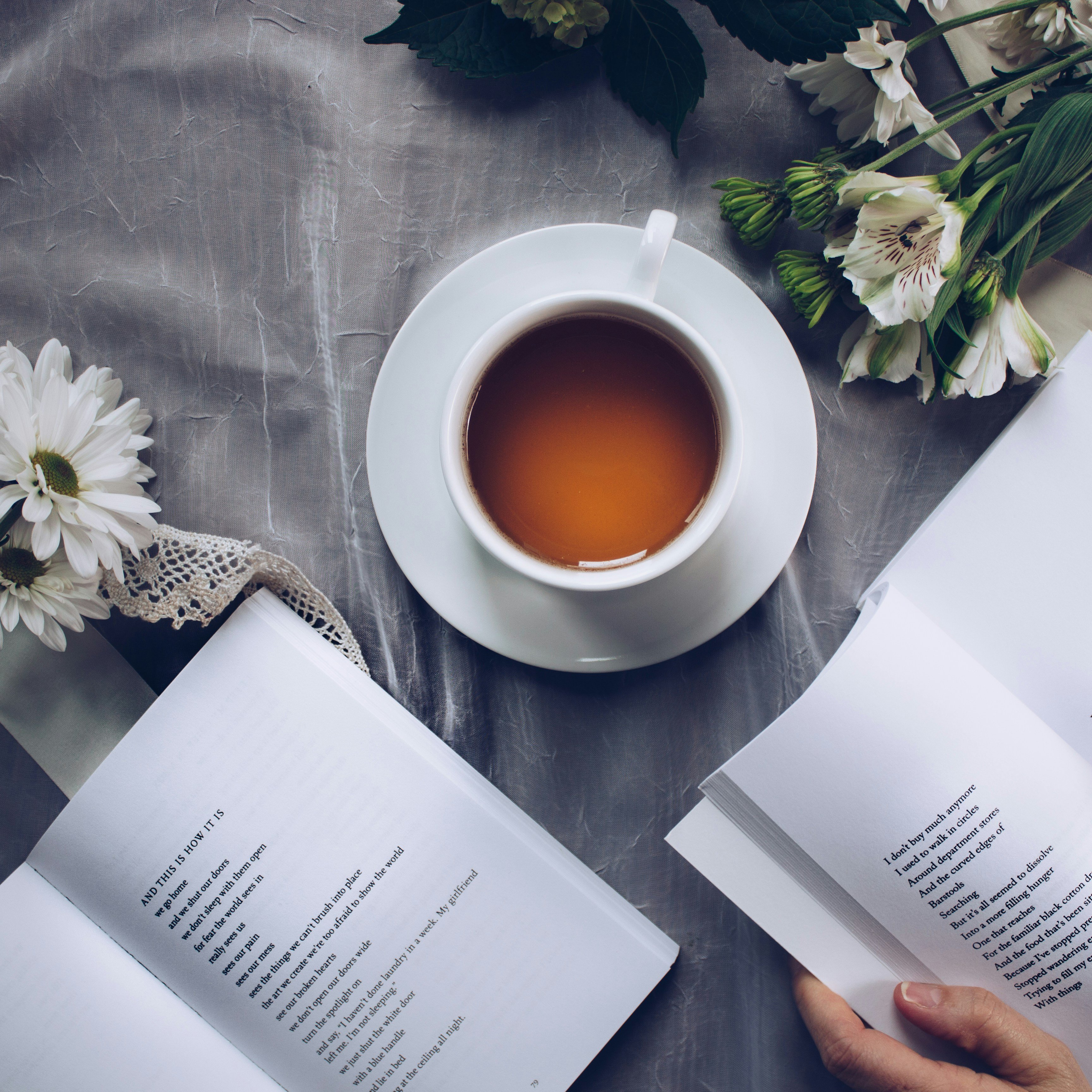 Woman reading a book with tea and flowers.