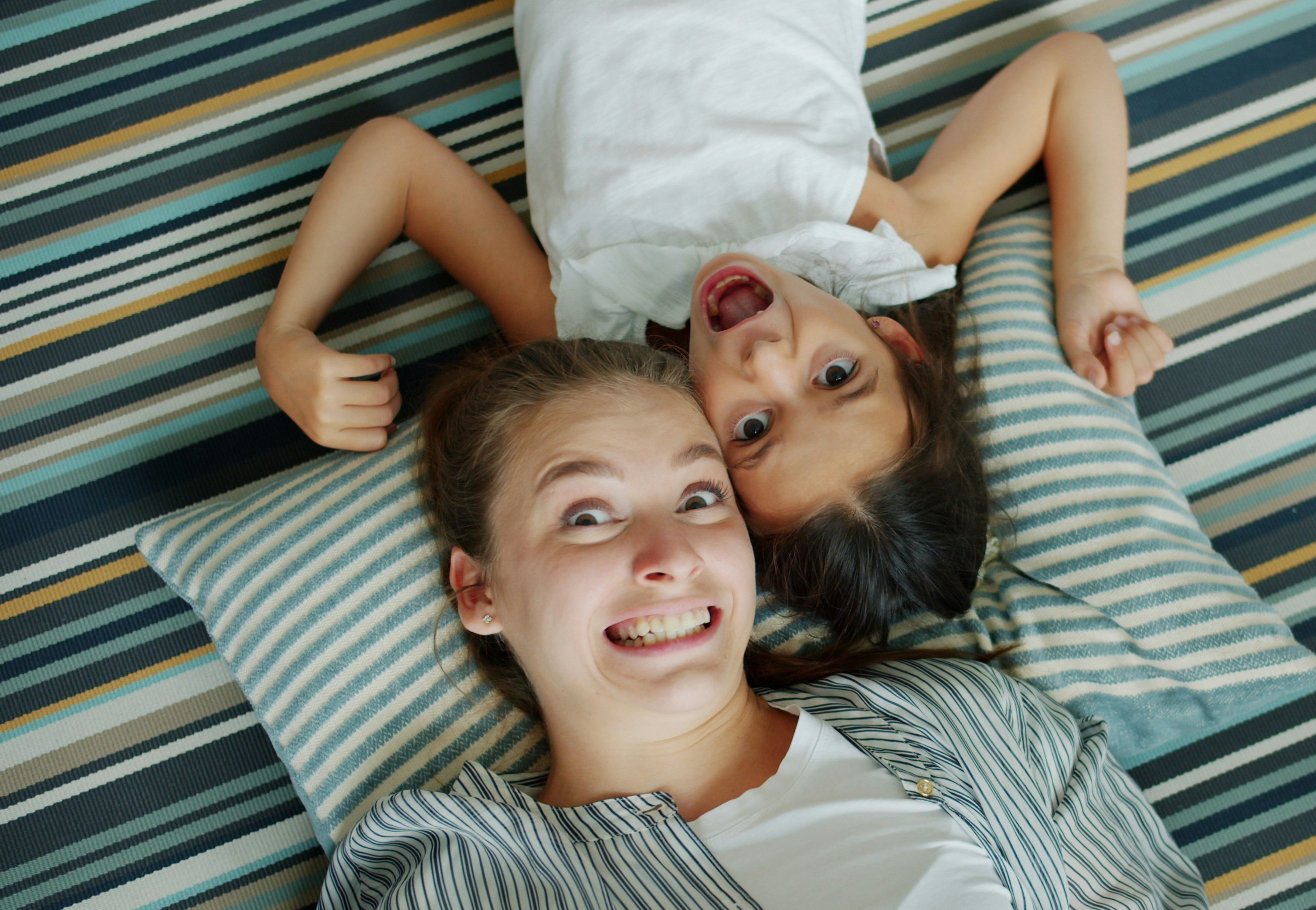 Top view of mother and cute daughter making funny faces lying on floor in apartment enjoying silly activity. Youth, entertainment and happy people concept.