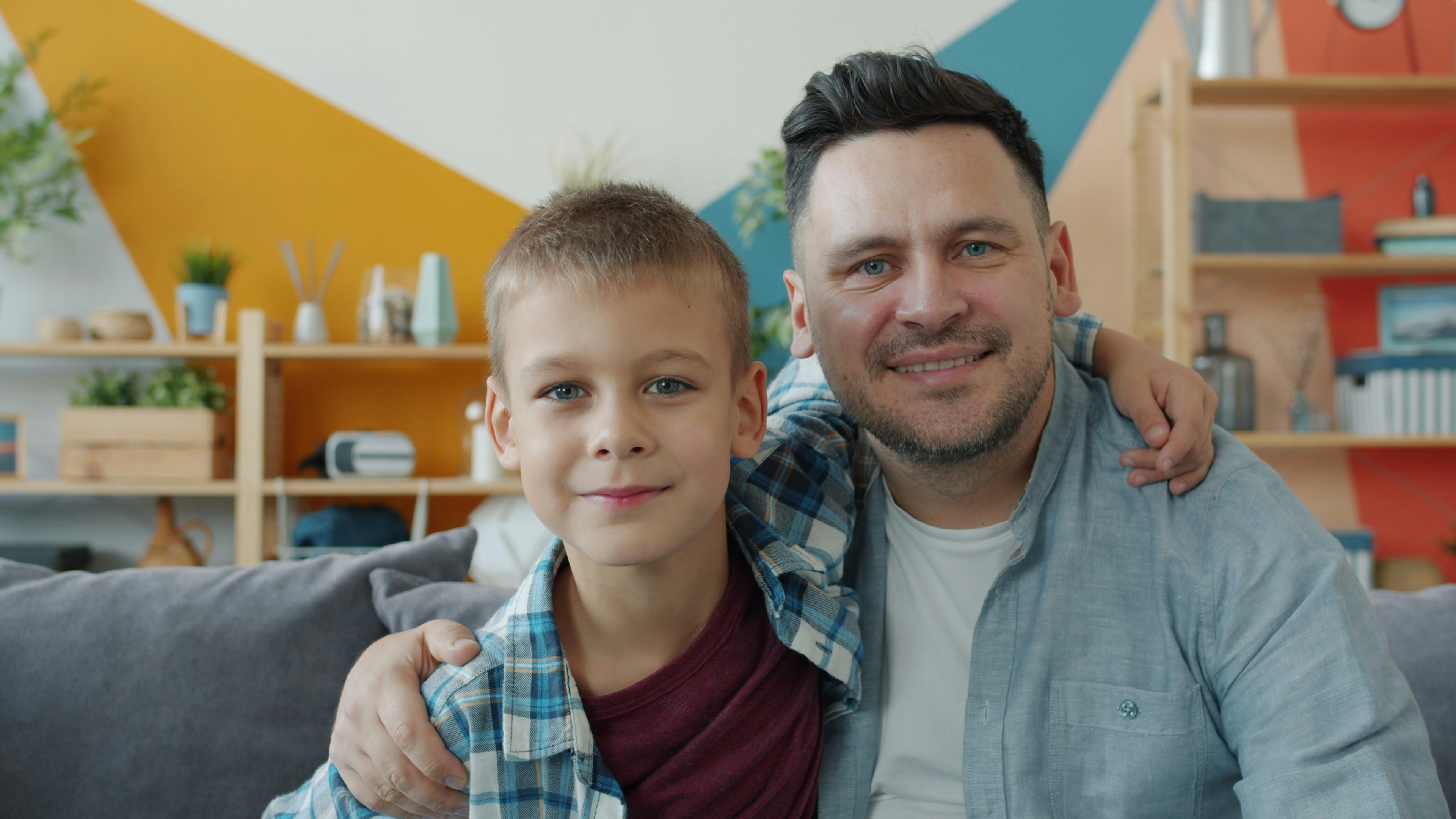 happy family dad and little boy smiling looking at camera in apartment sitting on couch together embracing. Love, fatherhood and people concept.