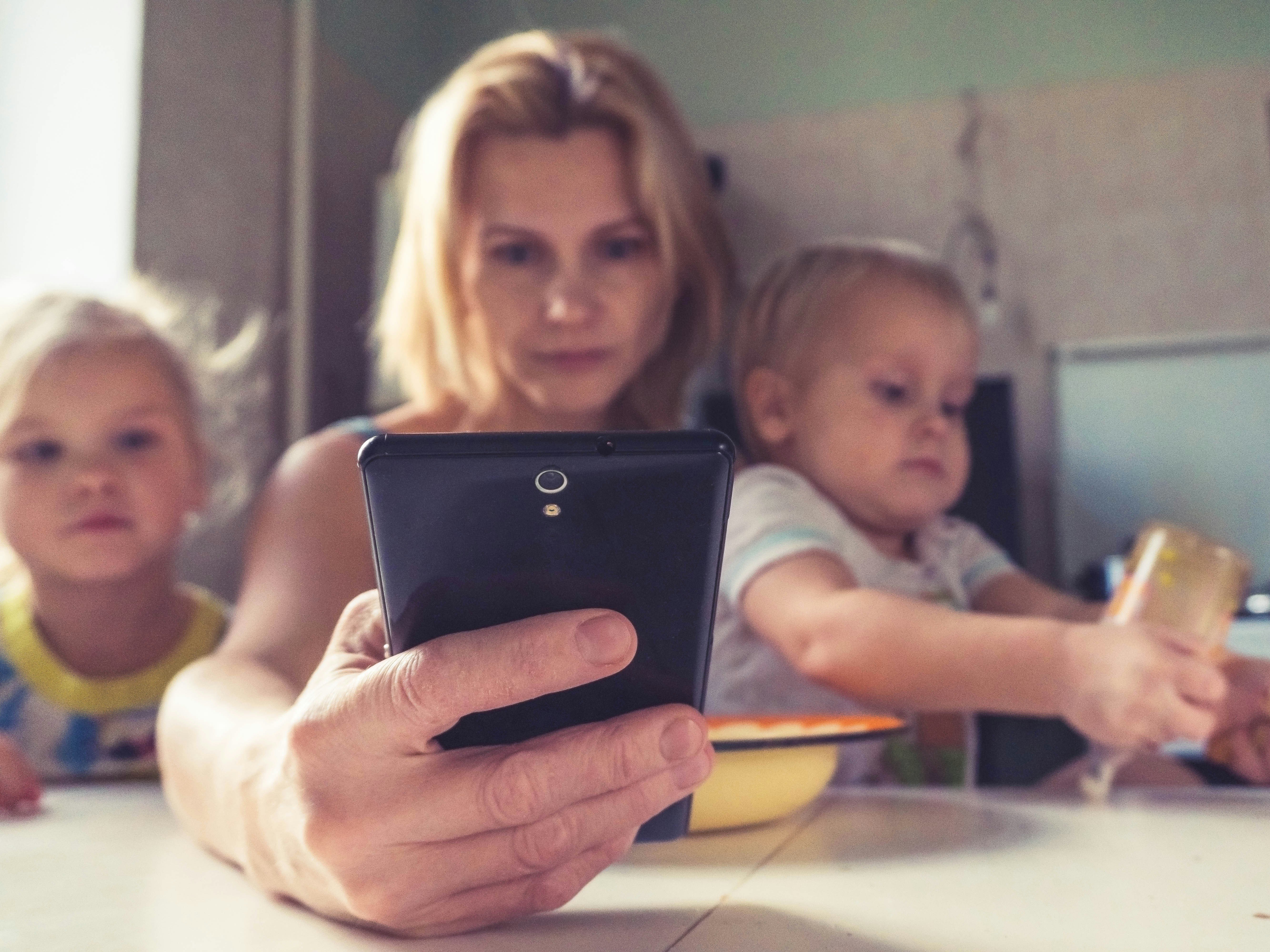 A woman uses smartphone while sitting with children, working mom
