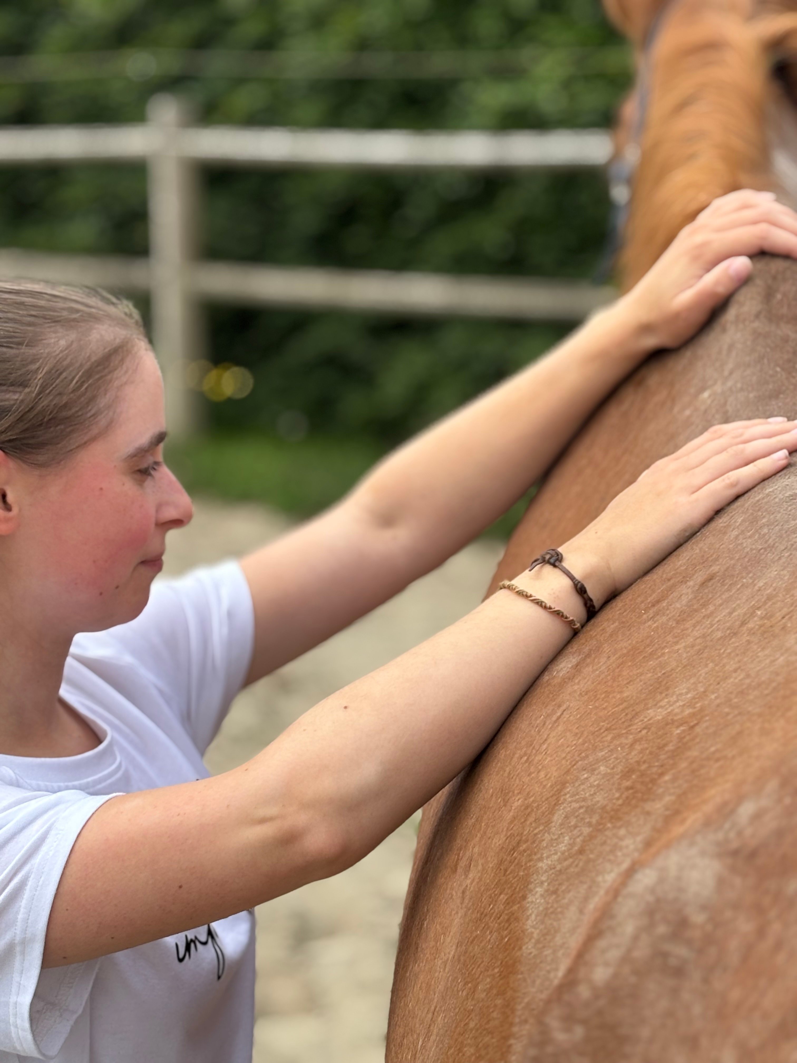 Cursist plaatst haar handen op de schouderzone van het paard tijdens een praktijkmoment