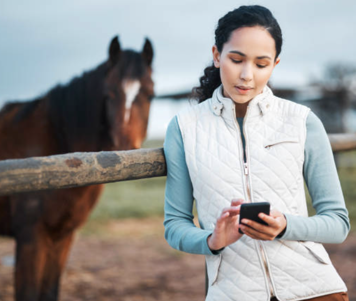 Paardeneigenares kijkt op haar gsm, klaar om haar affiliate-link te delen met andere eigenaars.